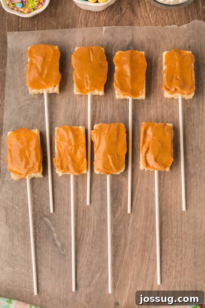 A Rice Krispies Treat Pop after being coated on one side with the warm, melted peanut butter and mini marshmallow mixture, laid back on waxed paper to cool slightly.
