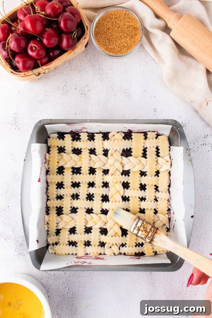 Sweet Cherry Pie Bars 11 Unbaked cherry pie bars with lattice crust being brushed with egg wash