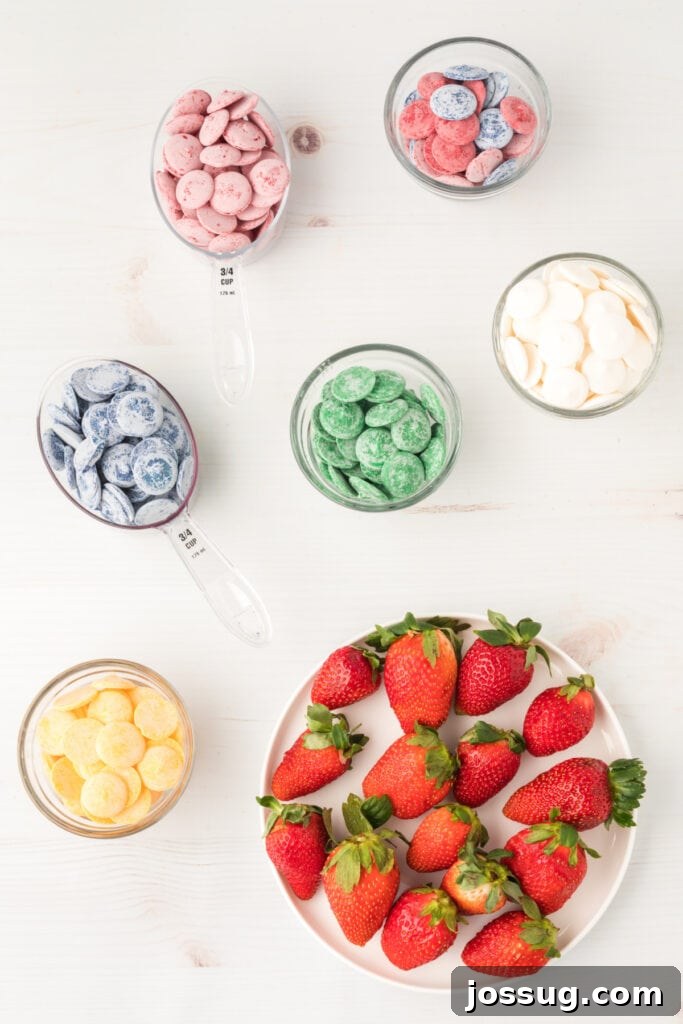 A selection of candy wafers in various colors, alongside fresh strawberries, laid out as ingredients for candy coated strawberries.