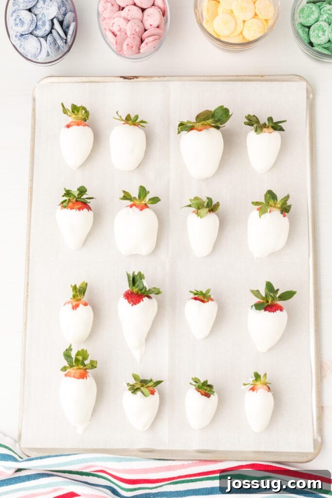 A strawberry freshly dipped in white candy coating, sitting on parchment paper.