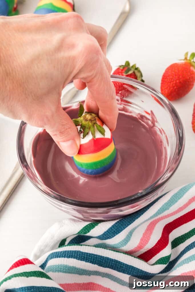 A hand gently dipping a strawberry into a bowl of melted purple candy melts.