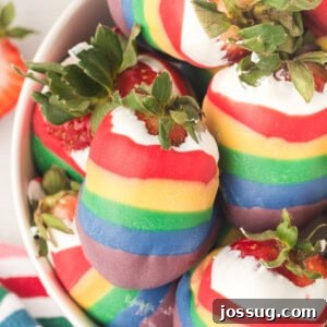 Closeup of rainbow candy coated strawberries stacked in a bowl, showing their vibrant layers.