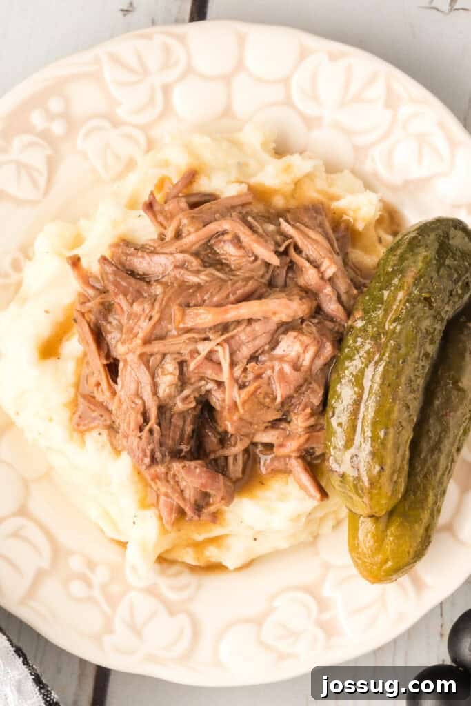 Zesty Slow Cooker Pot Roast 2 Plate of creamy mashed potatoes topped with savory dill pickle pot roast and whole pickles on the side, ready to serve.