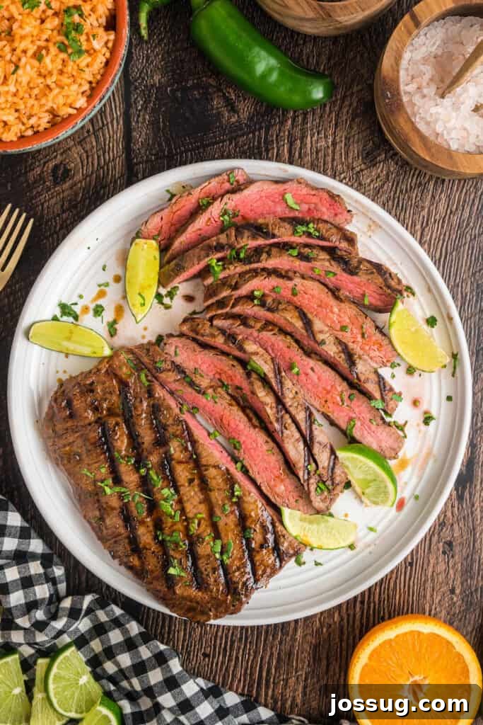 Flavorful Grilled Carne Asada 58 Overhead view of a platter with sliced carne asada garnished with lime wedges and cilantro, with small bowls of salsa and avocado nearby