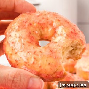 hand holding a vanilla cake donut with strawberry glaze