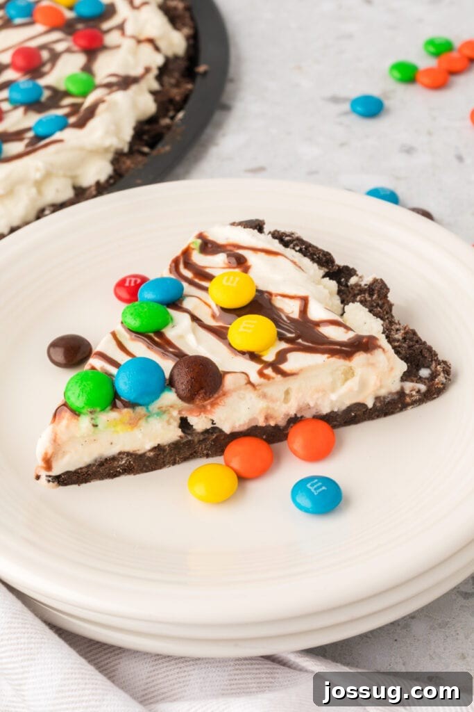 Dessert Pizza Dreams 3 A perfectly sliced wedge of ice cream pizza rests on a pristine white plate, surrounded by scattered M&M’s, with the full, mouth-watering pizza blurring in the background.
