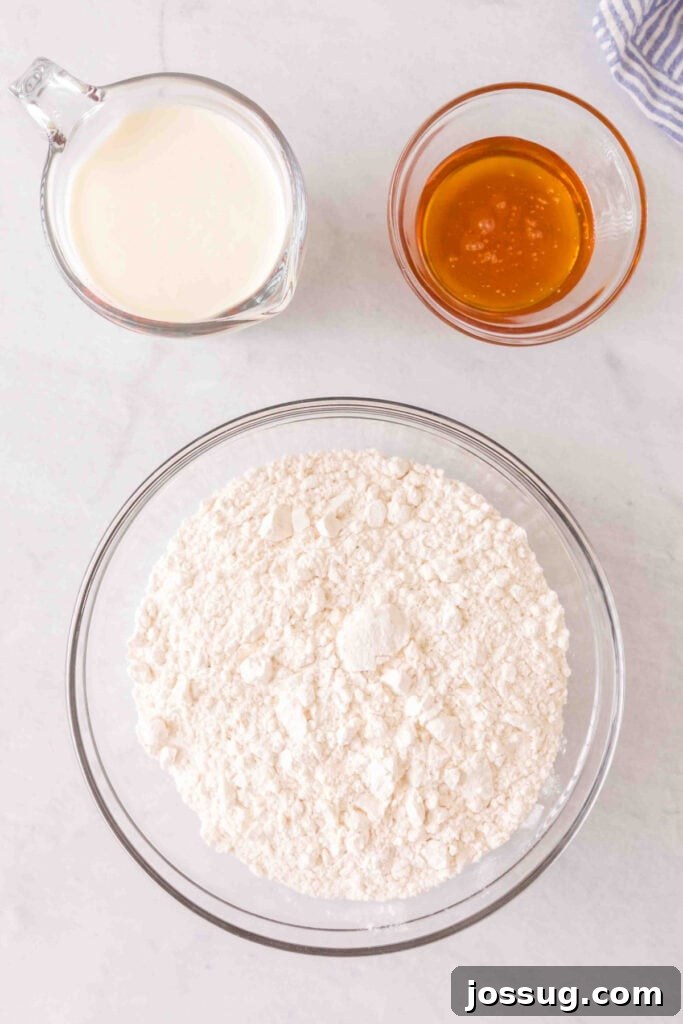 Amazing 3 Ingredient Scones 3 An overhead shot showcasing the three simple ingredients: a bowl of white flour, a small bowl of golden honey, and a glass jug of rich heavy cream, all ready for baking.