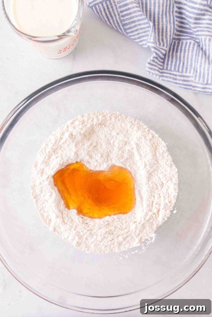 Amazing 3 Ingredient Scones 4 A stream of golden honey being poured into a large mixing bowl filled with white flour, with a jug of cream visible in the background, ready for the next step.
