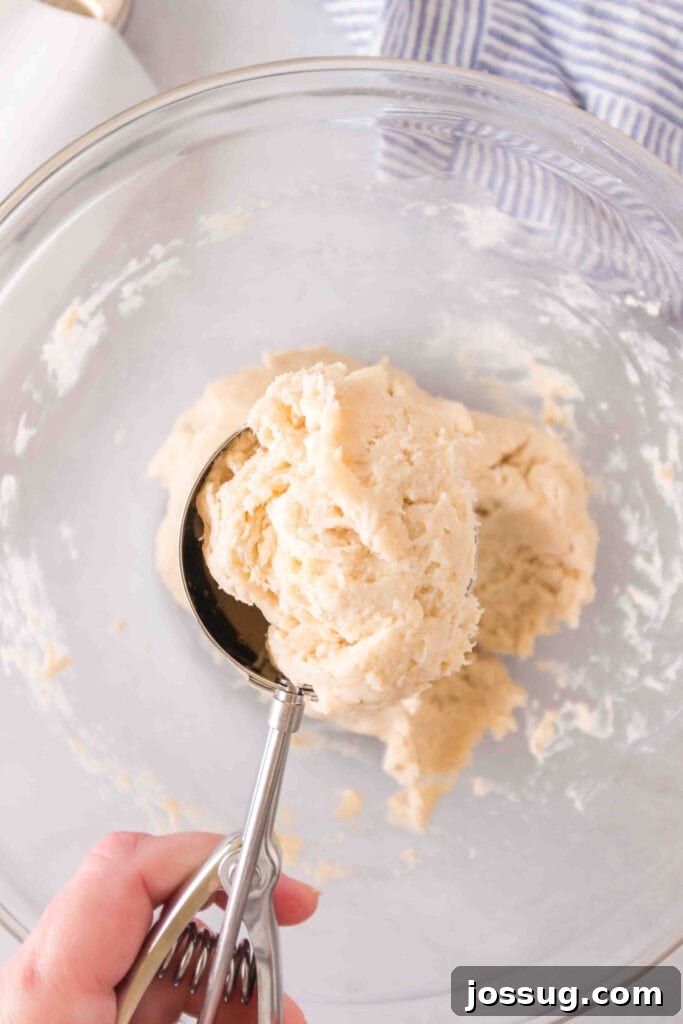 Amazing 3 Ingredient Scones 6 A large cookie scoop lifting a perfectly portioned mound of thick scone dough from the mixing bowl, showcasing its readiness for baking.