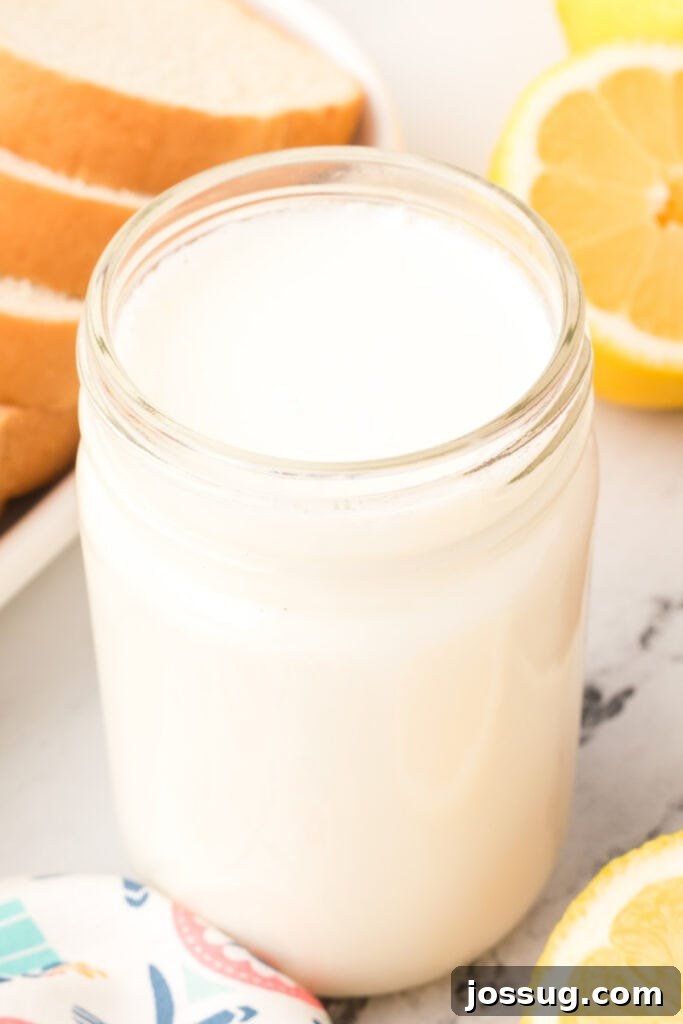 Close-up of a mason jar filled with buttermilk substitute beside fresh lemons, indicating a natural homemade solution.