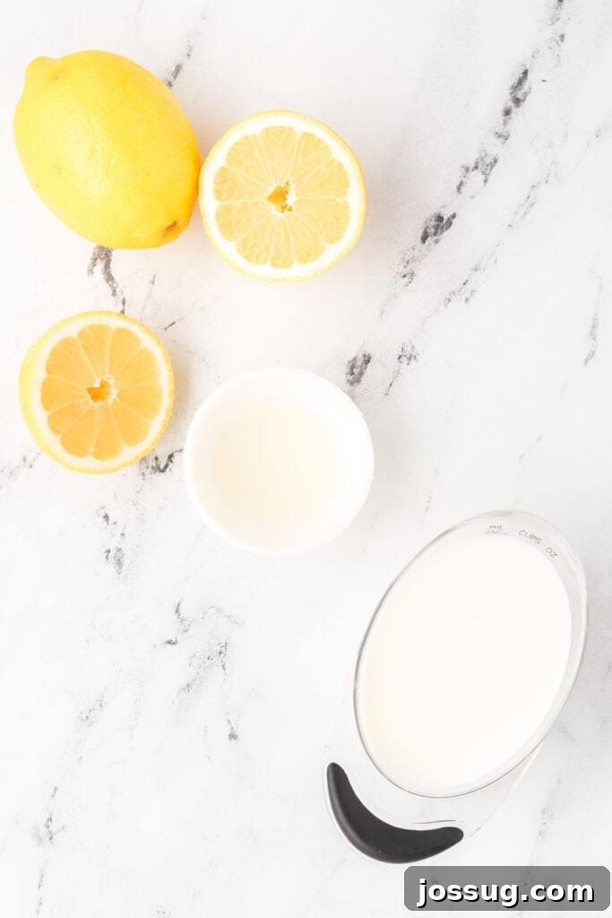 Whole and halved lemons with small bowls of lemon juice and milk on a pristine marble surface, illustrating the simple ingredients for buttermilk substitute.