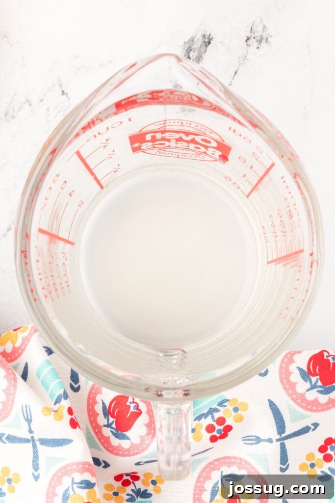 Overhead view of lemon juice at the bottom of a glass measuring cup, ready for milk to be added.