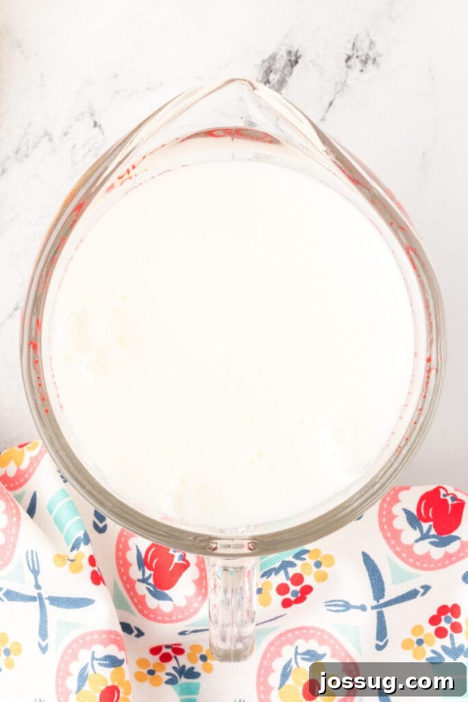 Overhead of milk added to the lemon juice and creating a thickened buttermilk substitute in a glass measuring cup, showing the curdling process.
