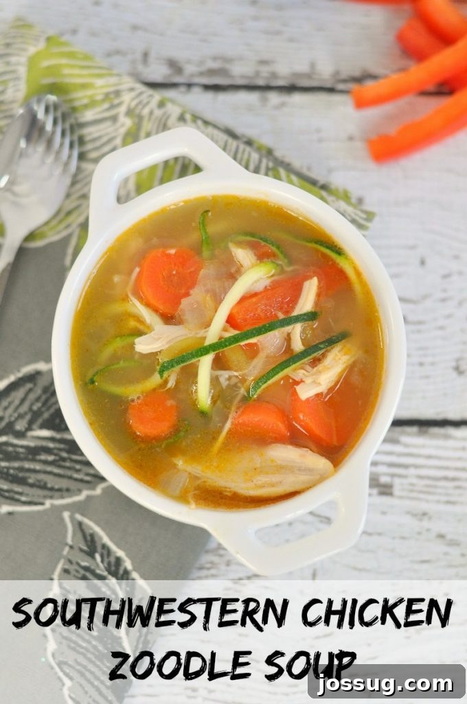 A steaming bowl of Southwestern Chicken Zoodle Soup, garnished with fresh cilantro and a lime wedge, in a rustic white bowl.