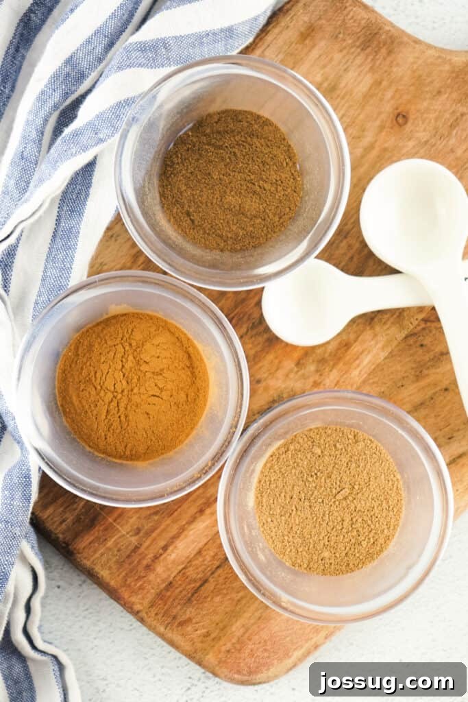 Overhead view of ground cinnamon, nutmeg, and allspice neatly arranged in small clear bowls, showcasing the individual components of the spice blend
