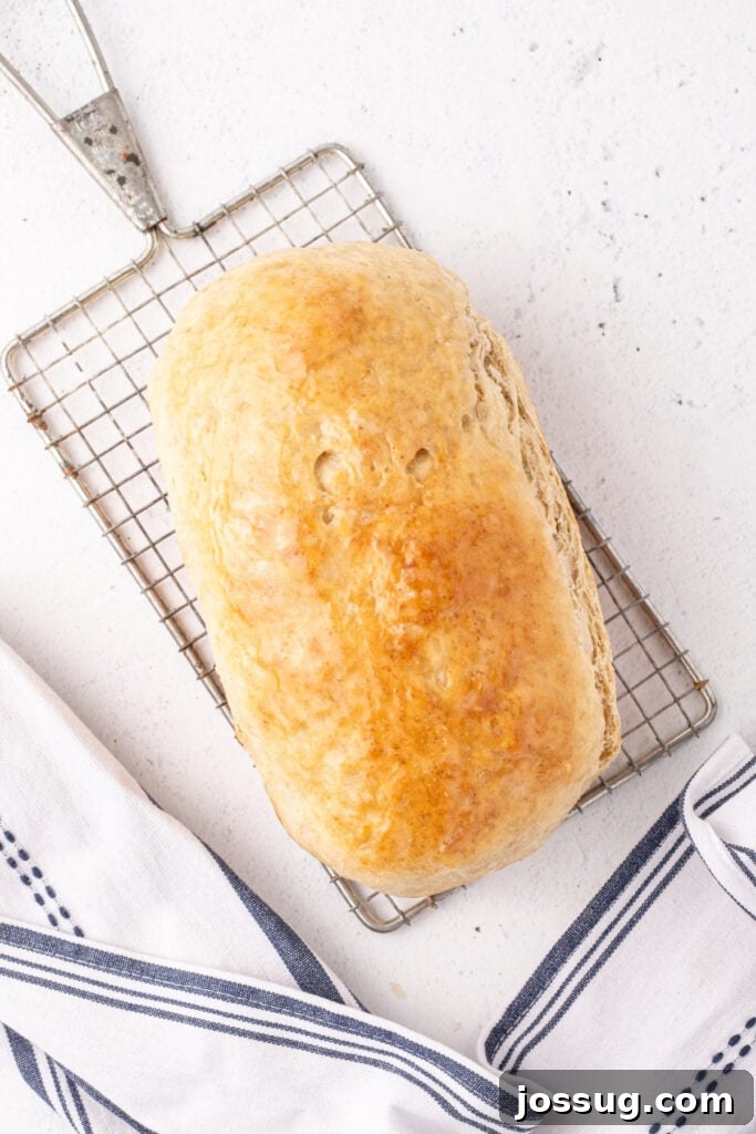 Freshly baked loaf of homemade bread cooling on a wire rack with a tea towel nearby
