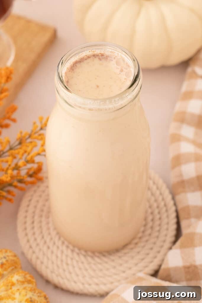 Glass bottle filled with homemade pumpkin spice creamer, elegantly placed on a textured coaster with autumn leaves in the background.