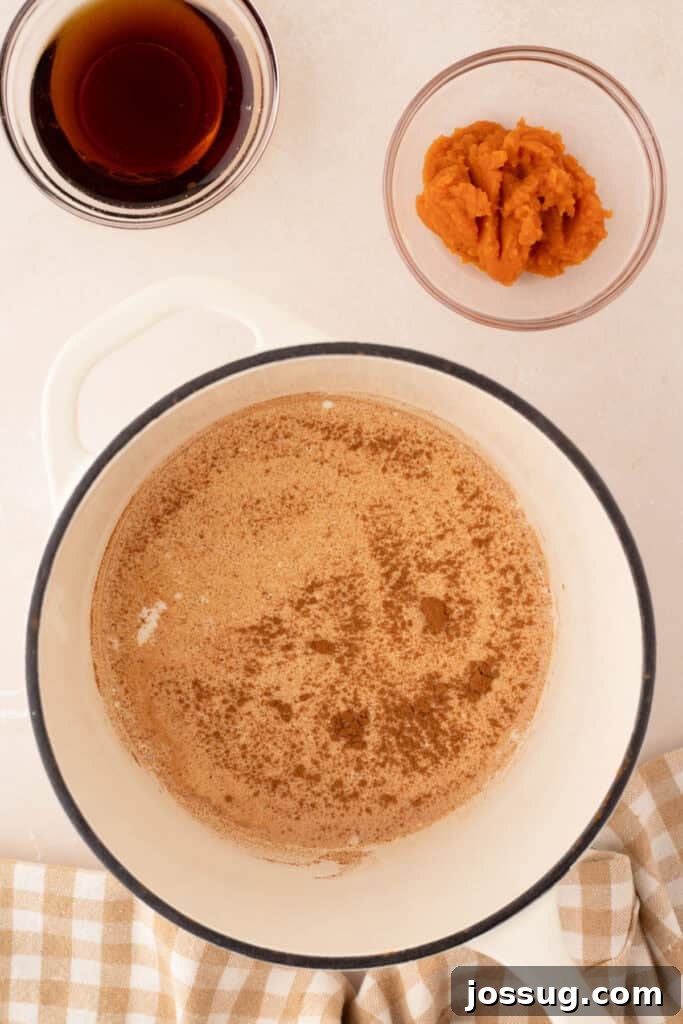 Pumpkin puree and maple syrup are measured out, positioned next to a saucepan where warming spices are just beginning to heat.