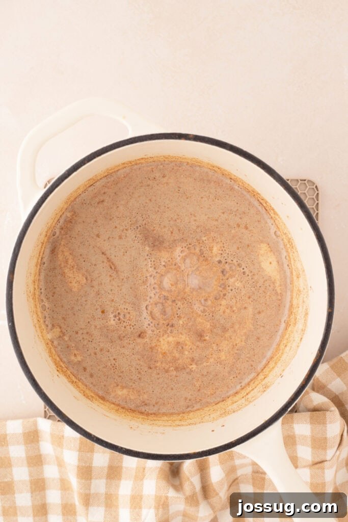 Homemade pumpkin spice creamer gently simmering in a pristine white Dutch oven, indicating it's nearly ready to be enjoyed.