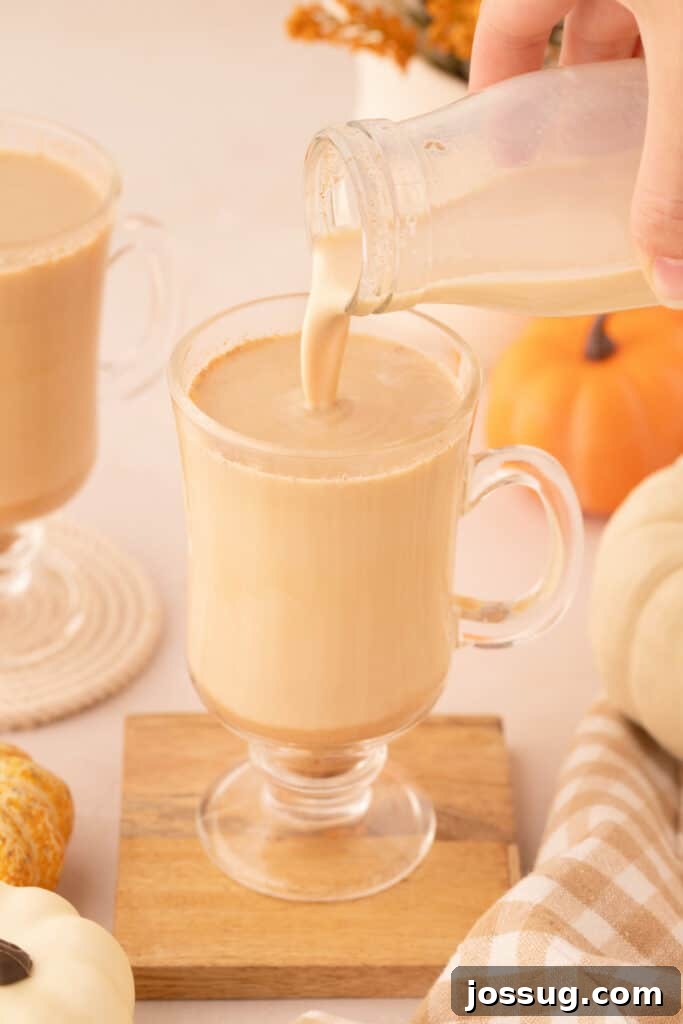 Rich pumpkin spice creamer being poured into a clear mug, surrounded by festive fall decorations, creating a cozy autumn scene.