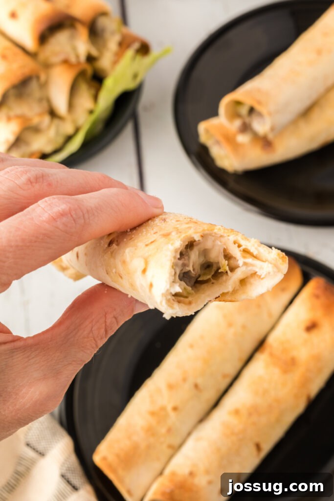 Hand holding a perfectly golden-brown Philly Cheesesteak Taquito