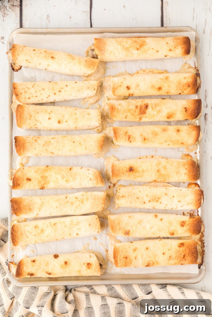 Crispy Philly Steak Rolls 3 Freshly baked golden-brown taquitos arranged neatly on a parchment-lined baking sheet