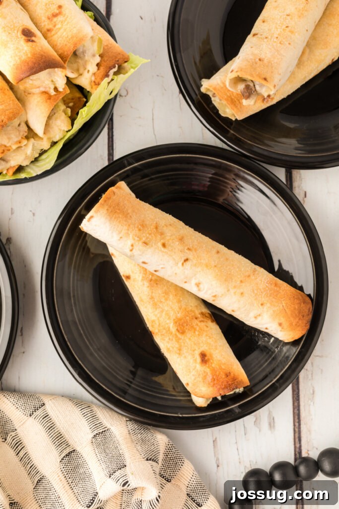 Crispy Philly Steak Rolls 4 Two perfectly baked Philly Cheesesteak Taquitos resting on a black plate, garnished delicately