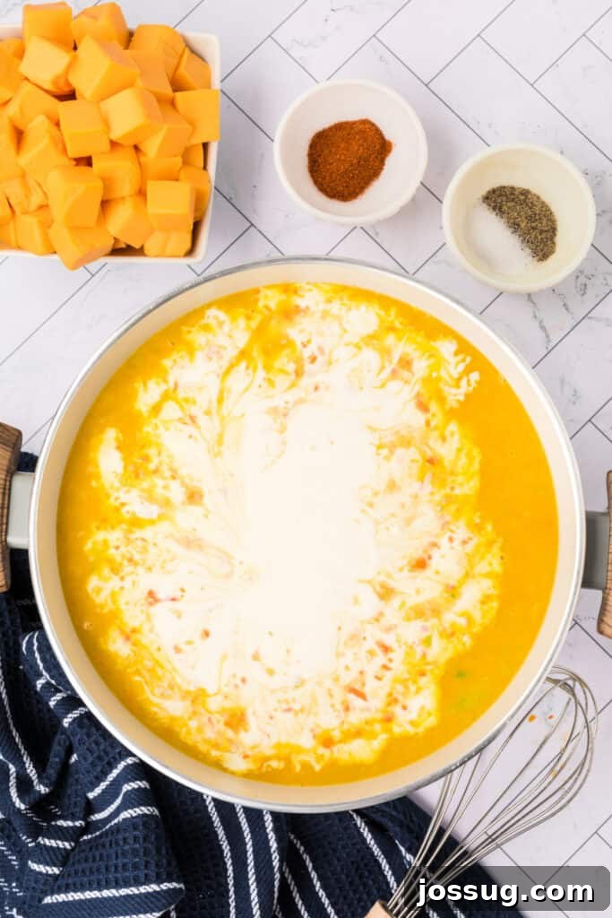 A generous swirl of heavy cream is being gently poured into the simmering vegetable and broth mixture in the pot, signaling the final stages of creating the soup's luxurious, creamy texture before the cheese is added.
