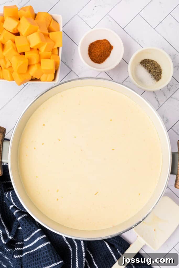 The smooth, creamy soup base is gently simmering in the pot, exuding a comforting aroma. Nearby, neatly arranged Velveeta cubes and bowls of cayenne and pepper sit ready to be incorporated, promising a rich, cheesy finish.