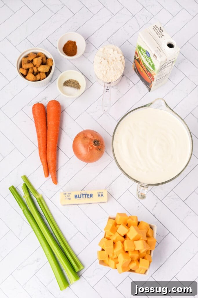 Overhead shot of all cheese soup ingredients meticulously laid out on a white tile background, including vibrant carrots, crisp celery, a yellow onion, perfectly cubed Velveeta, a stick of butter, a bowl of flour, and a carton of heavy cream, ready for preparation.