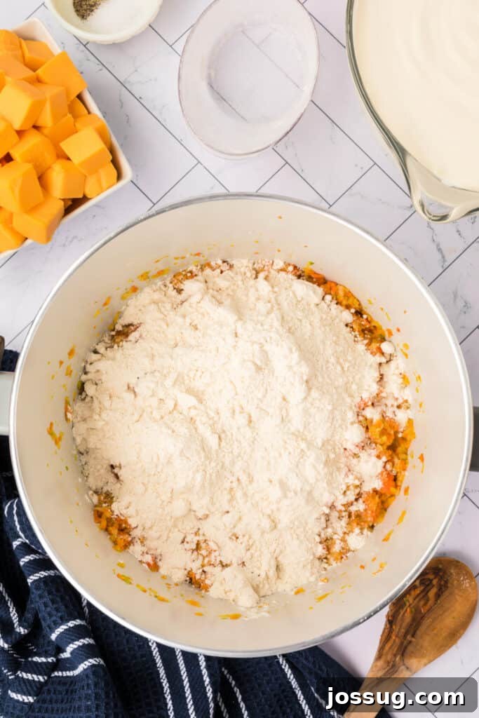 A generous mound of all-purpose flour has been carefully added to the sautéed vegetables in the pot, signifying the next critical step to create a foundational roux, which will thicken the soup.