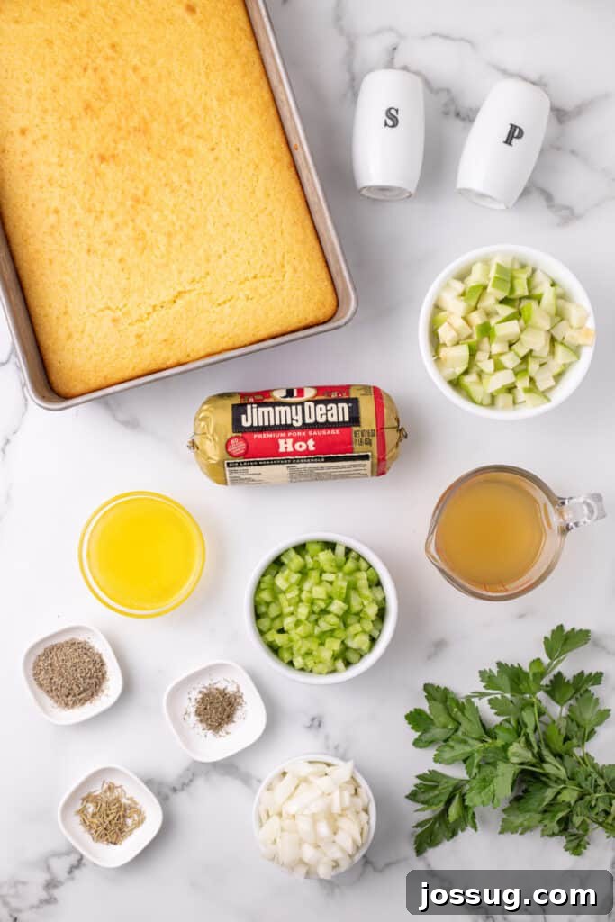 Homestyle Cornbread Dressing 3 Overhead view of baked cornbread in a pan with bowls of chopped apples, celery, onions, sausage, herbs, melted butter, and broth arranged on a marble surface.
