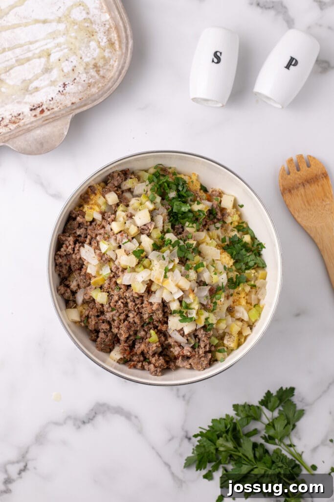 Homestyle Cornbread Dressing 8 Large mixing bowl filled with crumbled cornbread topped with cooked sausage, sautéed veggies, and chopped parsley before mixing.