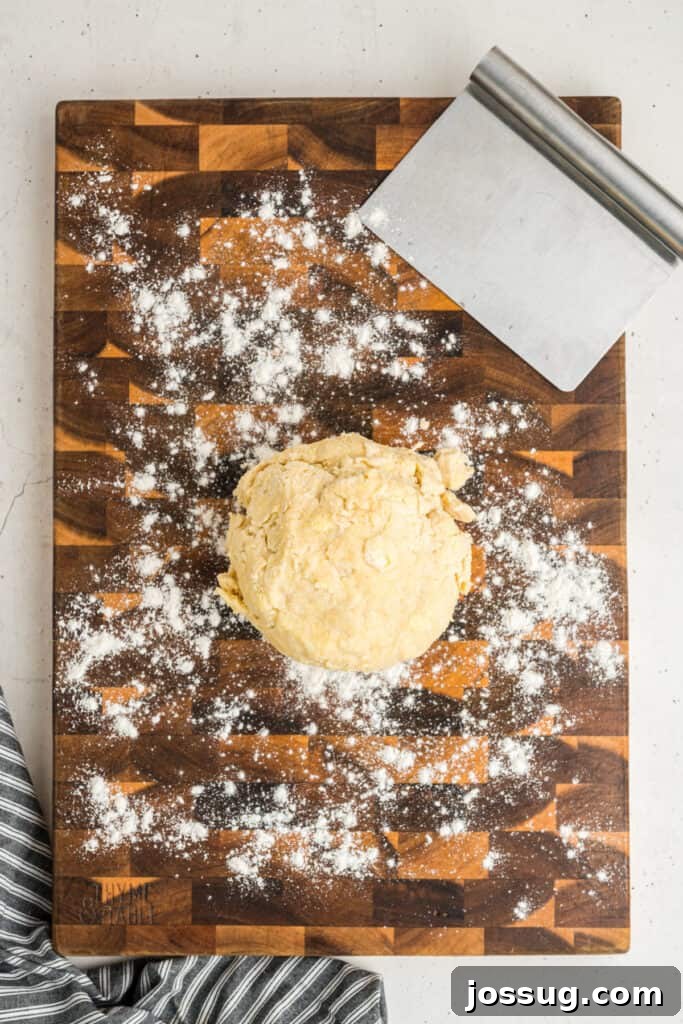 Ball of pie dough on a floured wooden board with a bench scraper beside it