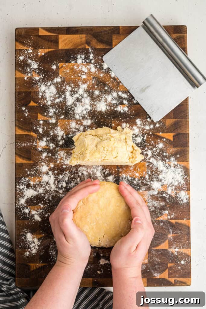 Hands shaping pie dough into a disc on a floured wooden board