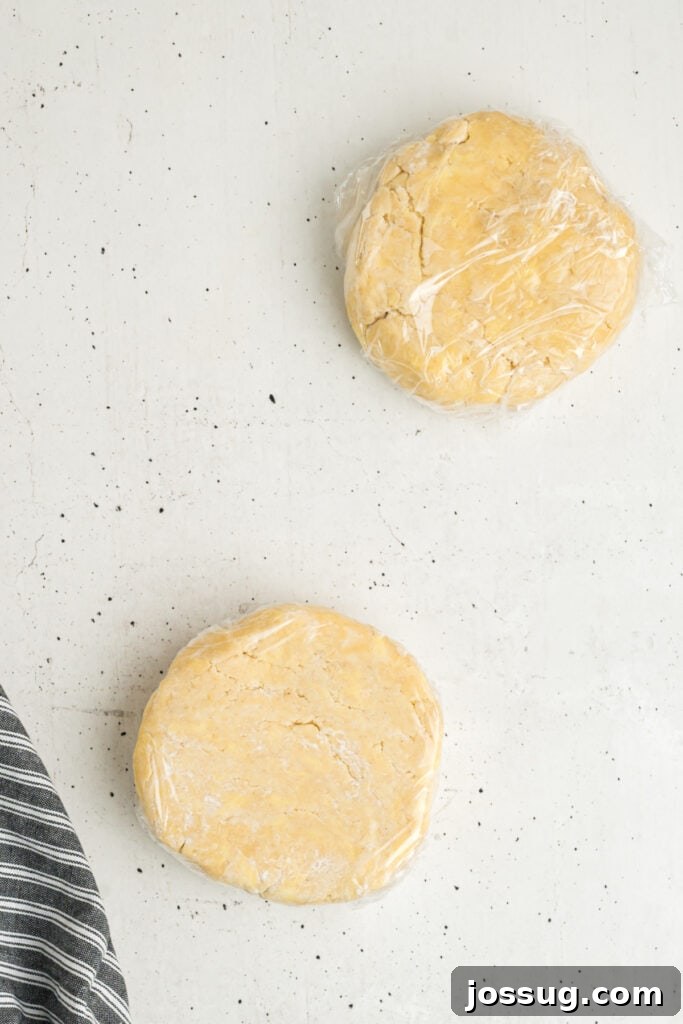 Two discs of butter pie crust dough wrapped in plastic wrap on a white surface
