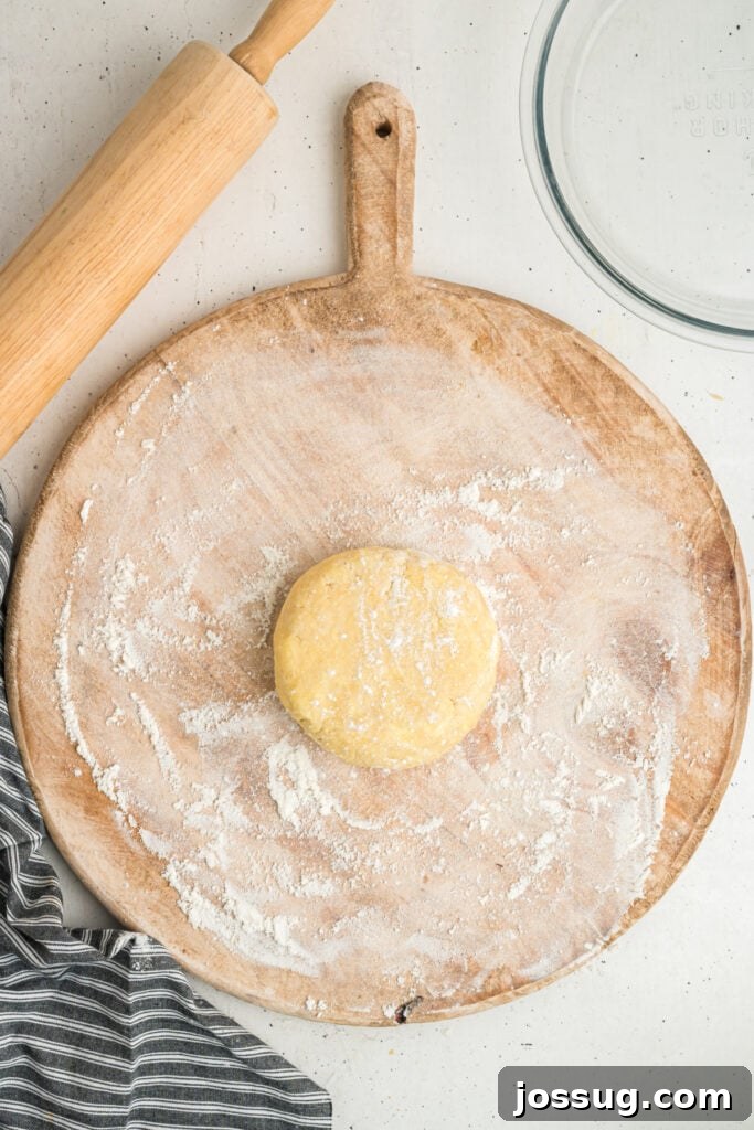 Disc of chilled dough on a floured wooden rolling board next to a rolling pin