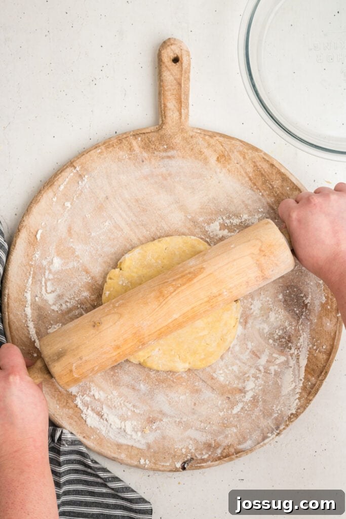 Hands rolling out pie crust dough with a wooden rolling pin