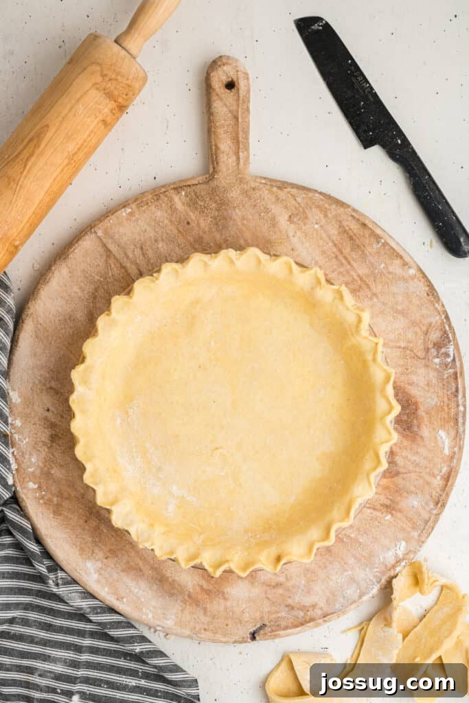 Pie crust with fluted edge formed in a pie dish on a wooden board
