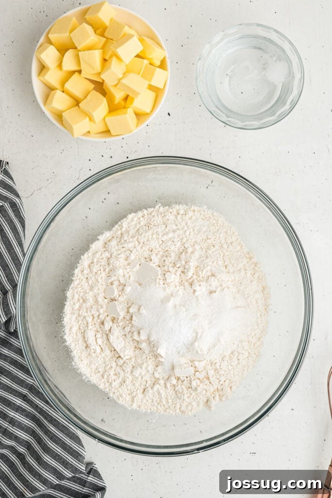Butter, water, and flour with salt and sugar in a mixing bowl on a light surface