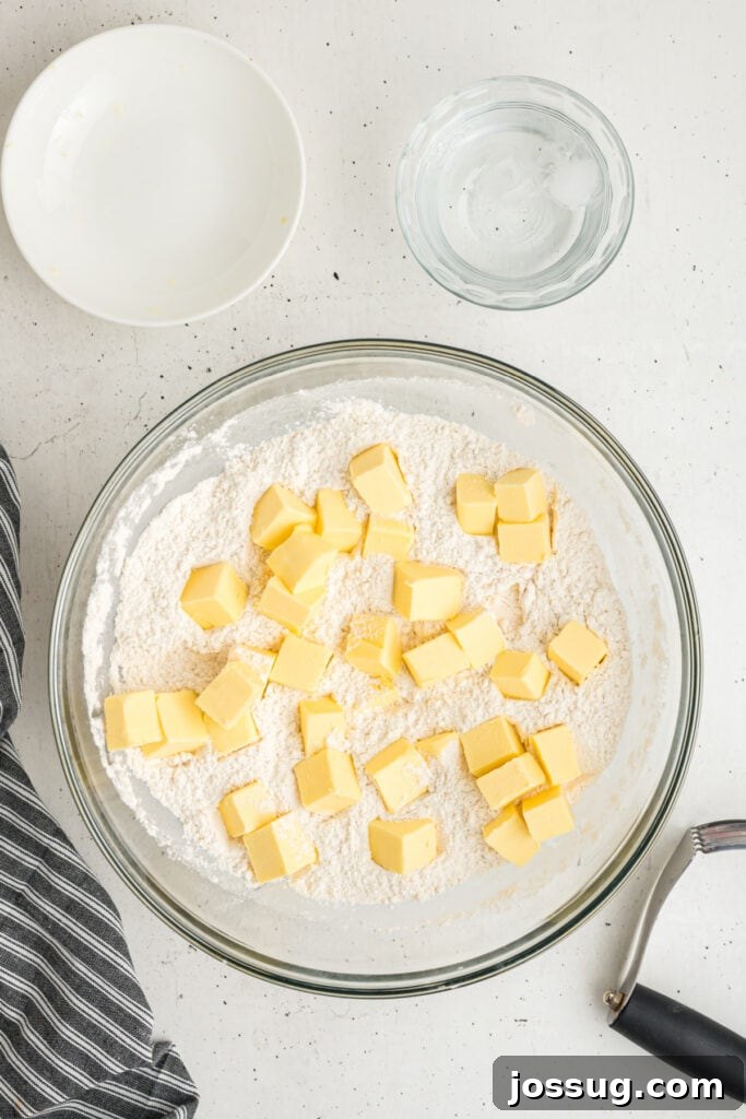 Cubed butter added to the flour mixture in a bowl with water and tools nearby