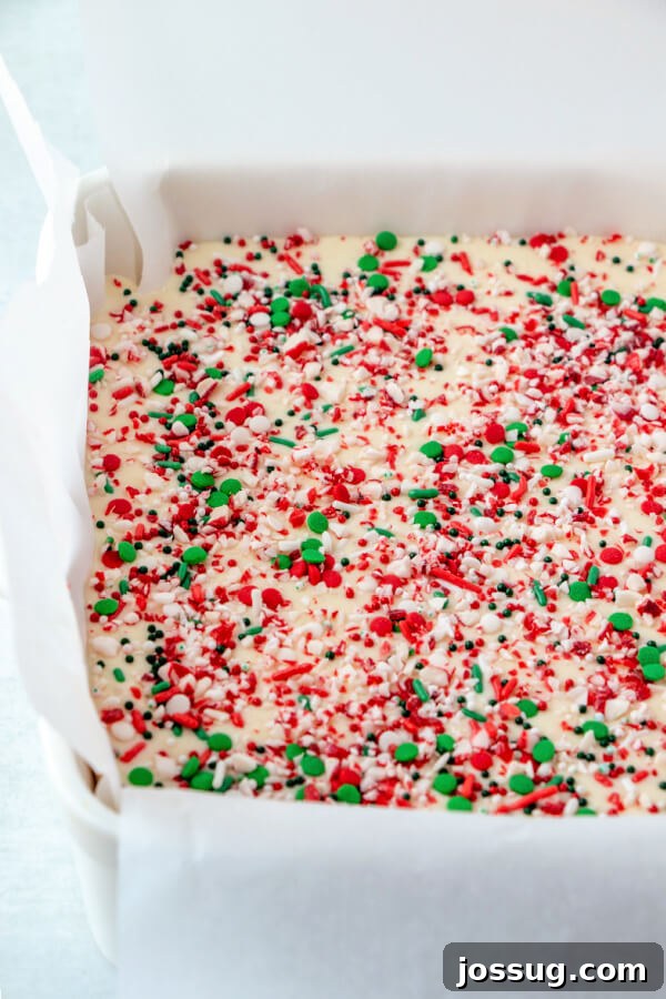 White chocolate peppermint fudge cooling and setting up in a square baking pan, topped with sprinkles.