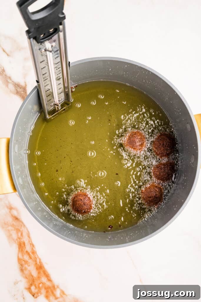 Chocolate donut holes frying in hot oil with thermometer visible