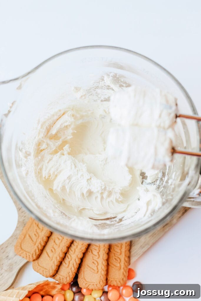Cream cheese being whipped until smooth in a glass bowl with mixer attachments visible, illustrating the first step of making the filling.