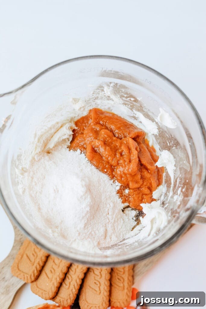 Pumpkin pie mix and cheesecake pudding mix added to whipped cream cheese in a bowl, demonstrating the combination of key ingredients.