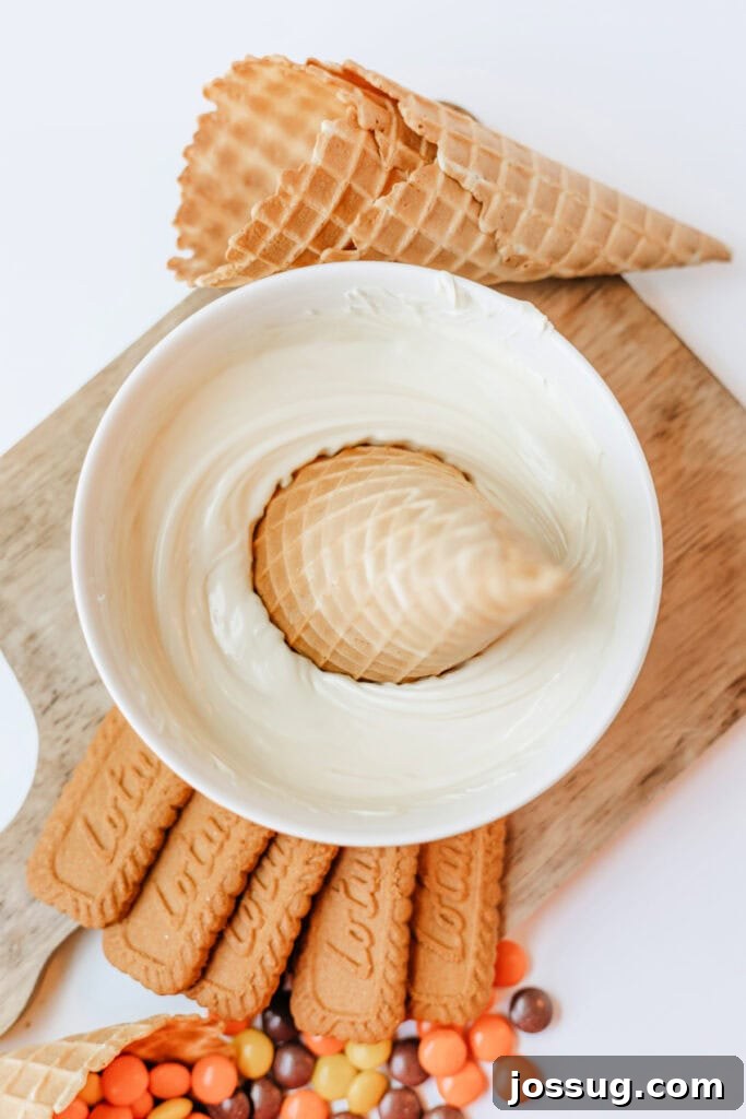 Waffle cone being dipped into melted white chocolate in a white bowl, showing the process of coating the cones.