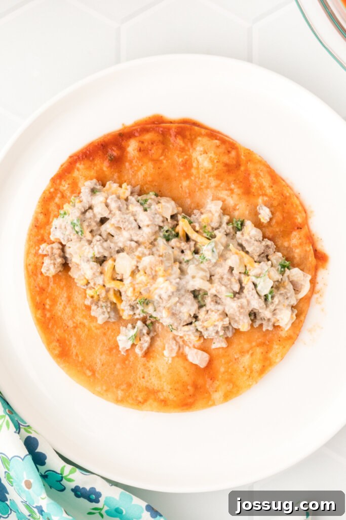 a corn tortilla being filled with ground beef mixture before rolling