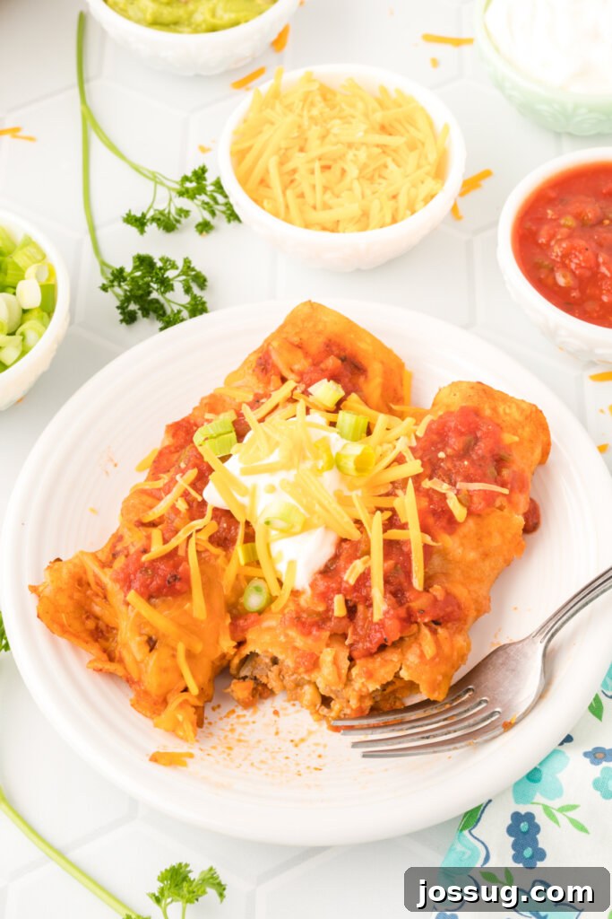 a white plate with two ground beef enchiladas, garnished with sour cream and cilantro