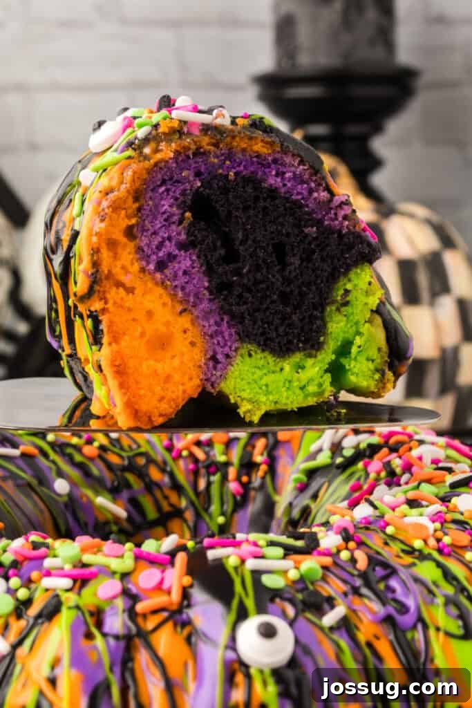 Bewitched Bundt Cake 2 Close-up slice of Halloween Bundt Cake showing orange, purple, black, and green layers with festive sprinkles.