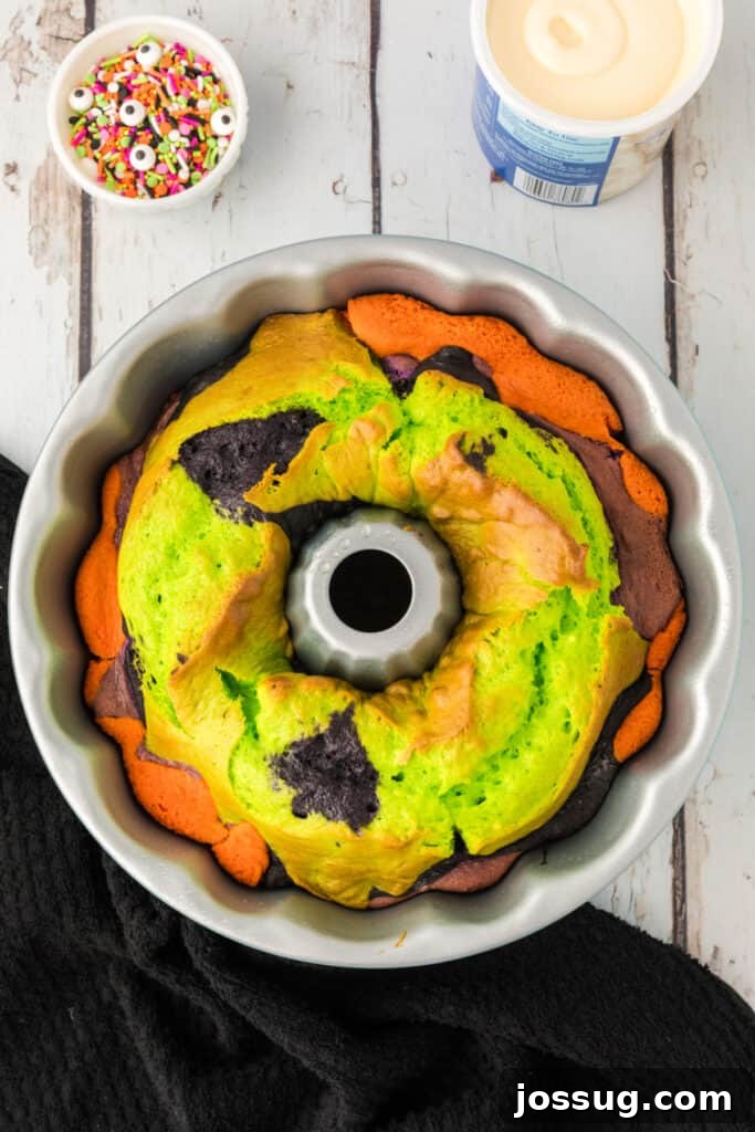Bewitched Bundt Cake 15 Freshly baked Halloween Bundt Cake in the pan showing vibrant orange, green, and black layers.